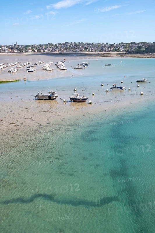 Over the shallow, turquoise water and moist sandy soil at low tide (low tide), with the shadows of currents and rocks visible in the water and numerous small boats dry in the background, Erquy, Saint-Brieuc Bay, Côtes-d'Armor Department, Brittany Region, France
