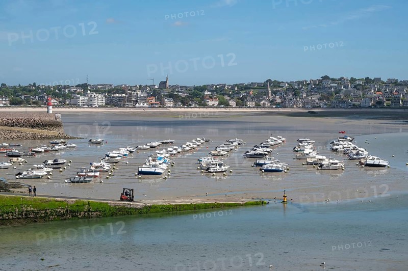 At low tide (low tide), a large collection of small motorboats lies neatly in rows on the moist harbor sand, while in the background the densely built town center of Erquy with church tower and the small lighthouse at the entrance to the harbor is visible, Erquy, Saint-Brieuc Bay, Côtes-d'Armor, Brittany region, France