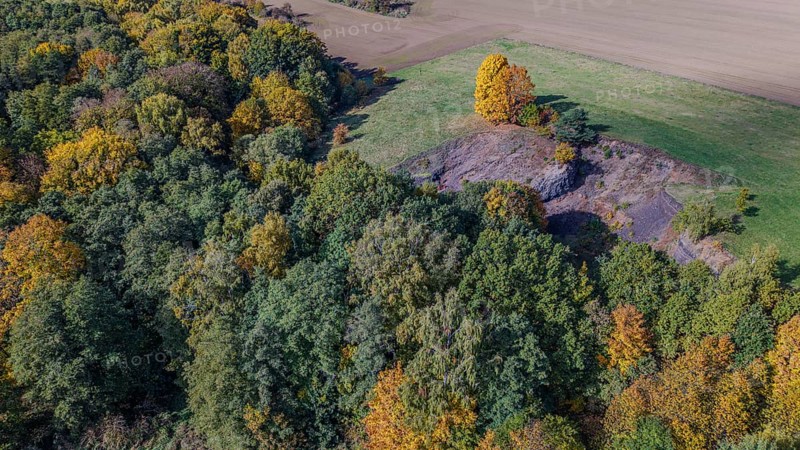 The scene shows an autumnal landscape with colorful foliage. An extinct volcano is surrounded by trees, while the surrounding area glows with soft colors. Železná hurka, Czech Republic