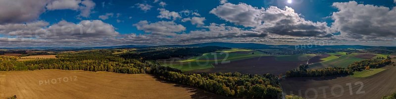 A breathtaking landscape with vast fields and deep blue skies. Sunlight shines onto the green area. Clouds gently pass by. Železná hurka, Czech Republic