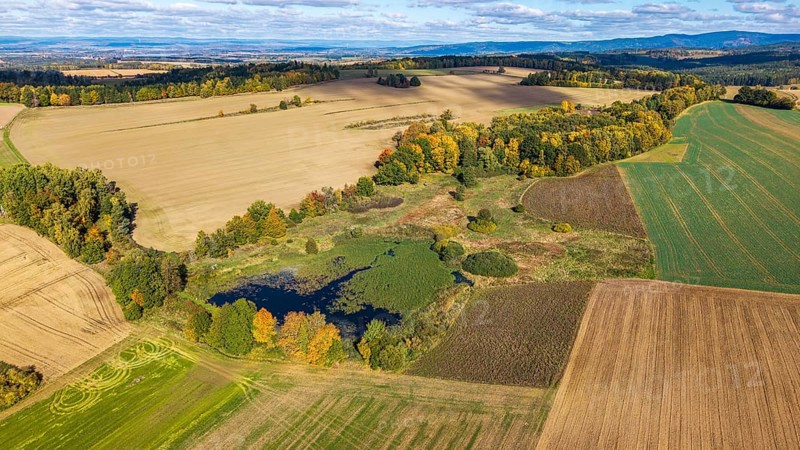 Colourful autumn colors characterize the rural scene with a small pond surrounded by meadows and fields. Nature is in full splendor under blue skies. Železná hurka, Czech Republic