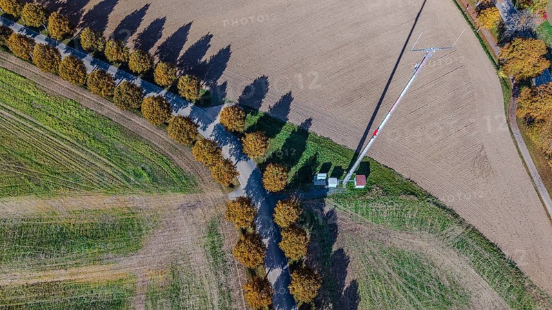 An antenna mast can be seen in a field in the middle of an autumn environment. The trees along the trail cast long shadows in the afternoon sun. Bad Neualbenreuth, Upper Palatinate