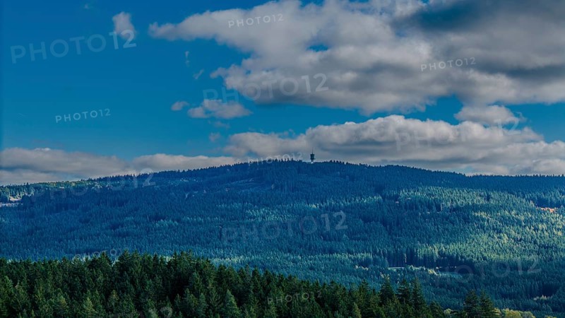 A green, wooded hill in the Bohemian Forest is visible under a blue sky with few clouds. Nature is calm and inviting, ideal for hikers. Dylen, Czech Republic