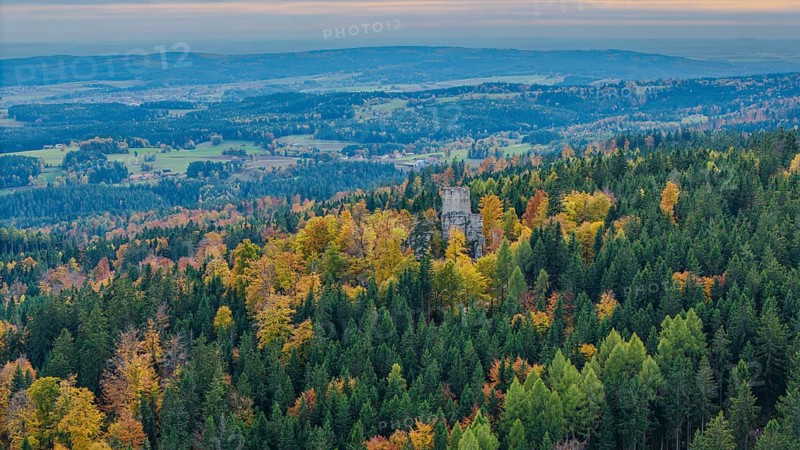 The ruins of Weissenstein Castle rise above a colorful forest whose leaves glow in autumn. The rolling hills and the wide valley create a picturesque landscape. Friedenfels, Upper Palatinate