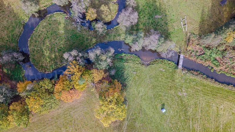 The scene shows a quiet river flowing through a picturesque meadow. Autumn colors of the trees and a small bridge complement the quiet landscape. Falkenberg, Upper Palatinate