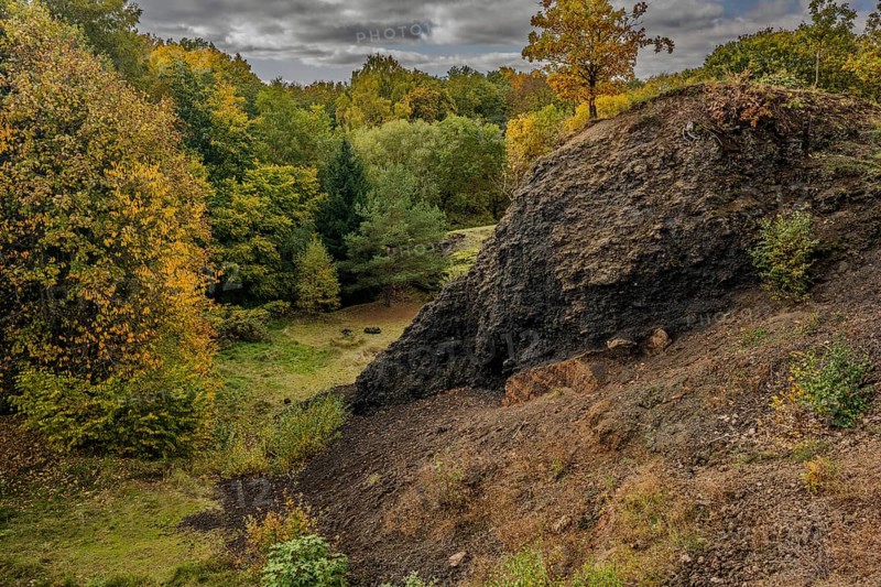 The scene shows an extinct volcano in autumn. Colourful trees surround a dark slope, while the sky is covered with grey clouds. A quiet place in nature. Železná hurka, Czech Republic