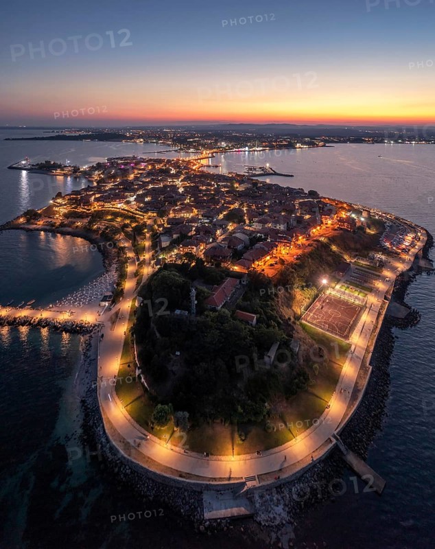 Historic peninsula illuminated at twilight, surrounded by calm sea waters. Aerial view to old town of Nessebar, Bulgaria night time