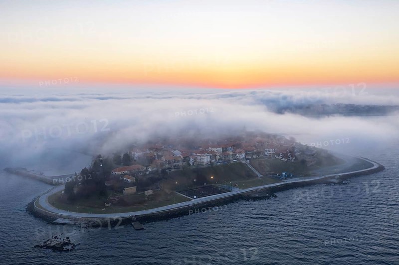 An island surrounded by mist at sunrise with calm waters. Aerial view to thick fog descends over the Nessebar, Burgas, Bulgaria