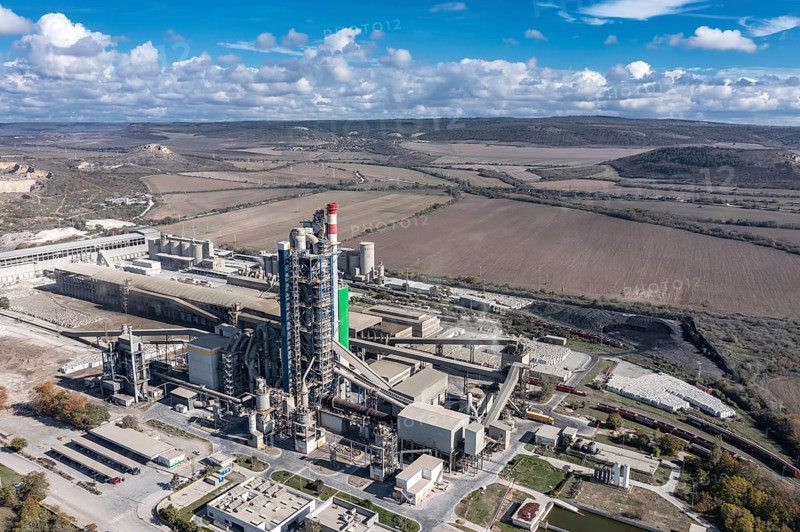 Aerial view of a sprawling industrial complex with rural fields in the background. Aerial view to cement plant near to Devnya, Varna, Bulgaria. Devnya cement plant