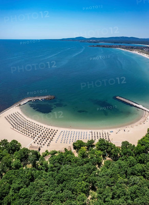 Scenic beach with lined umbrellas beside lush greenery and an expansive ocean. Aerial view to beautiful Perla beach near to Primorsko, Bulgaria