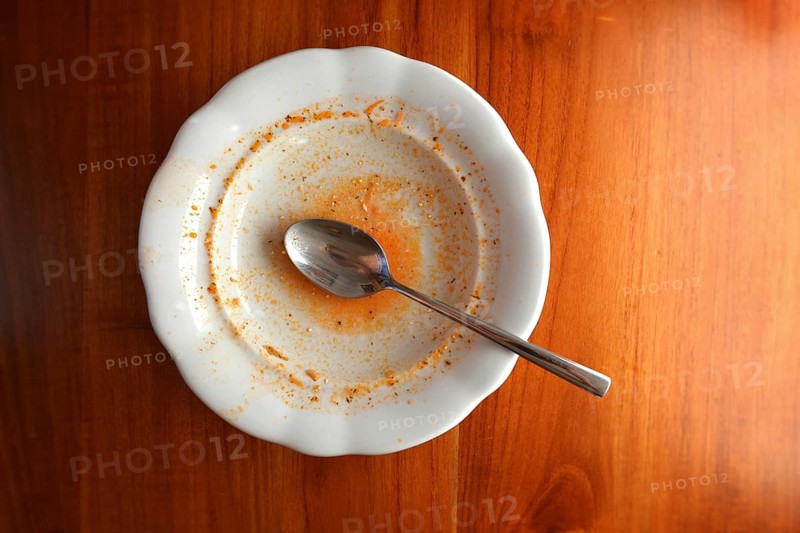 Empty white plate with spoon on wooden table, flat lay top view, red leftovers from soup or sauce Prague Czech republic
