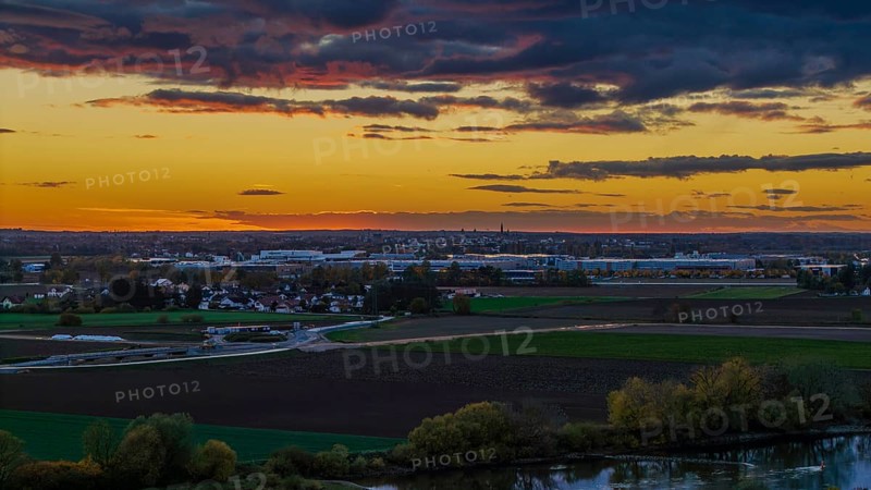 At sunset, the city of Straubing is painted in warm colors. The Danube flows calmly, while the clouds in the sky turn orange and pink and the landscape is illuminated. Straubing, Lower Bavaria