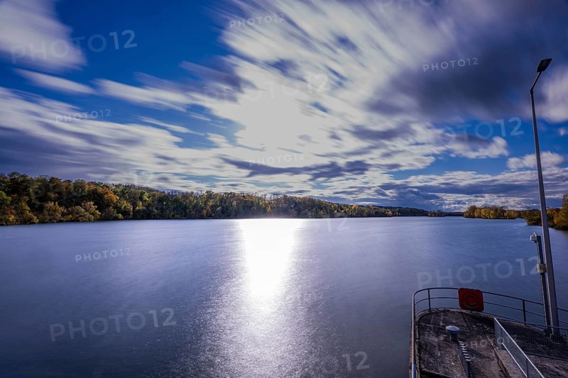 A quiet river stretches under a cloudy sky. The clouds move gently while the sunlight makes the water surface sparkle. Landau an der Isar, Lower Bavaria