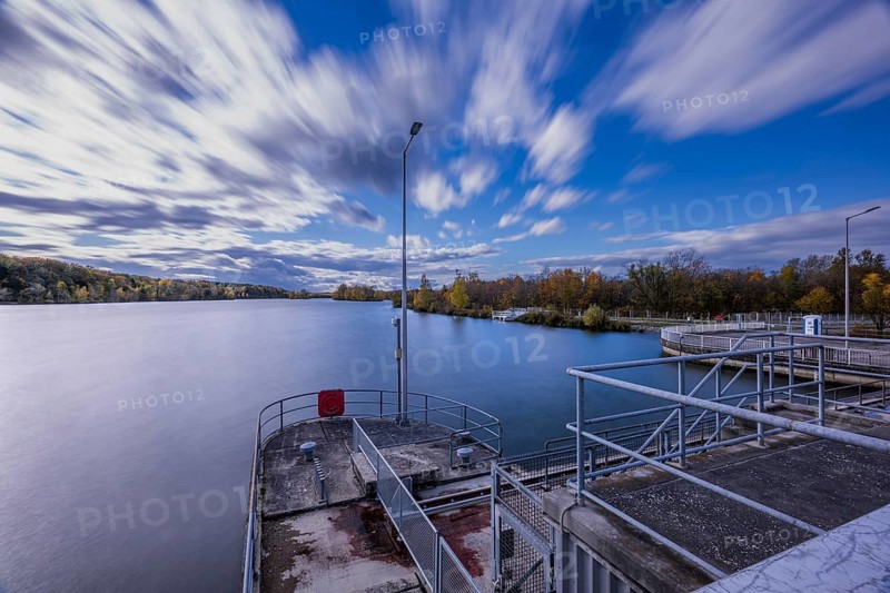A beautiful view of a peaceful river in cloudy weather. Trees on the shore show autumnal colors, while clouds pass by quickly. Landau an der Isar, Lower Bavaria