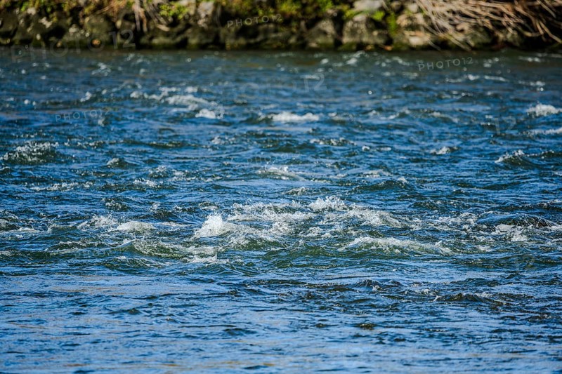 The clear water surface of a river shows soft waves that are created by the movement of the water. The surrounding area looks peaceful and natural. Landau an der Isar, Lower Bavaria