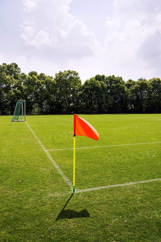 Orange vivid corner flag on fresh green football ground, trees in background, sunny summer day Prague Czech republic