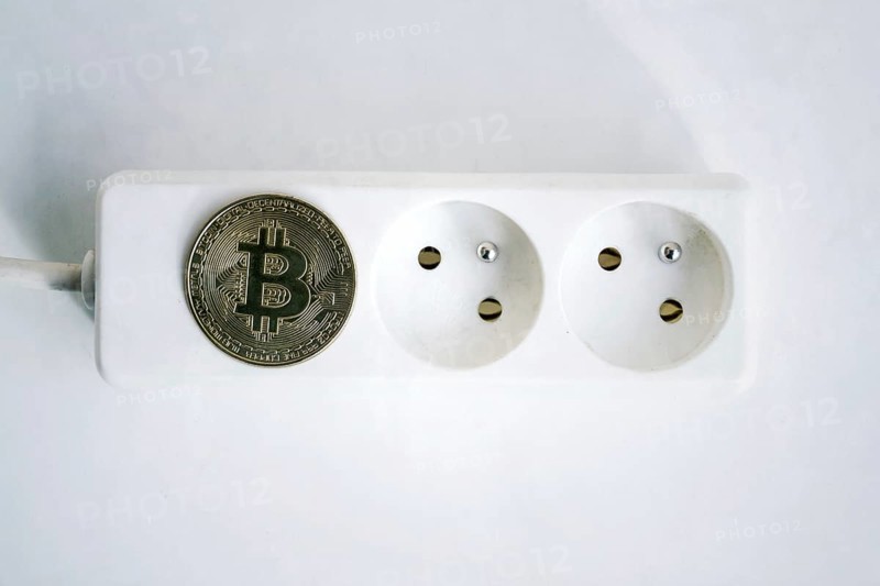 Bitcoin coin lying on power strip extension cord with two empty sockets, cryptocurrency investing, energy consumption and footprint concept, isolated on white background Prague Czech republic