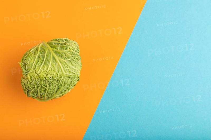 Green lettuce on blue and orange pastel paper background. Top view, copy space, flat lay. healthy food, vegetable, minimalism
