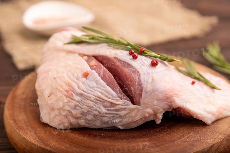 Raw Turkey Thigh with spices and rosemary on cutting board on brown wooden background and linen textile. side view, close up, selective focus