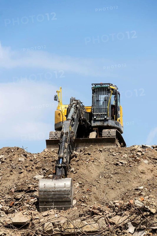 Yellow construction digger, excavator on demolition site stand on debris, sunny day clear blue sky, Prague, Czech republi