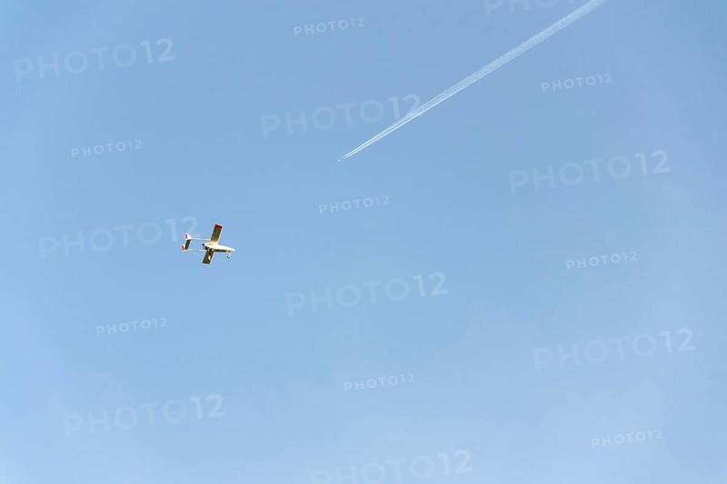 Unmanned aerial vehicle surveillance drone with light and camera flying, sunny summer day, drone delivery concept, copy space on clear sky, condensation trails and airplane in background Pisek Czech republic