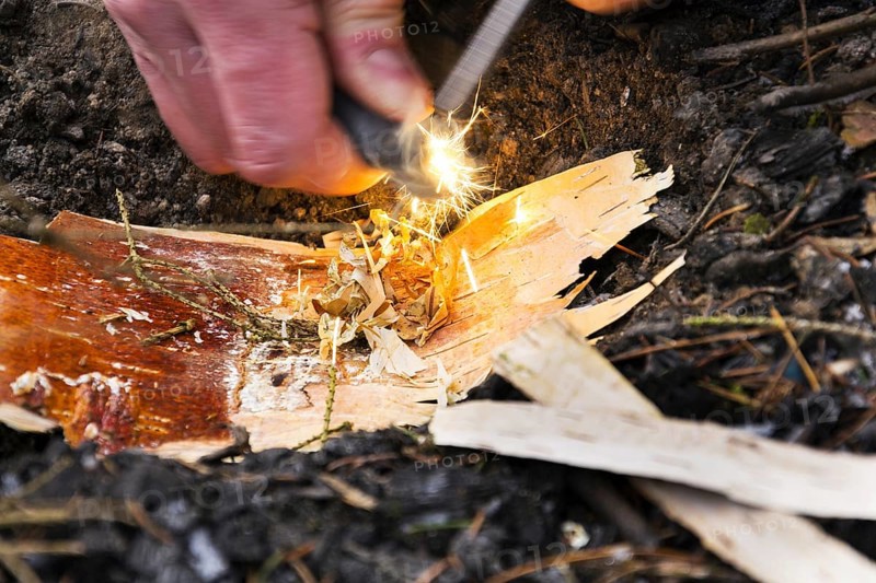 Male hand starts fire with magnesium fire steel, fire striker