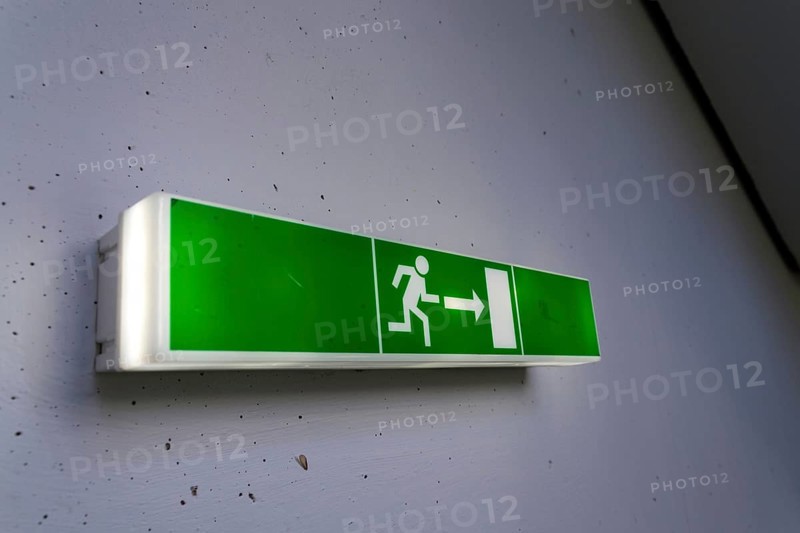 Green shining escape exit sign on white concrete wall