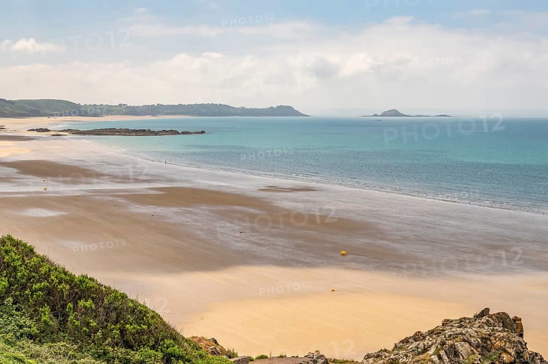A panoramic view from the Sentier Littoral cliff path shows the vast, shallow bay of Erquy and its large, rocky foothills at low tide and a wide, humid sandy beach in the center, Erquy, Cotes-d'Armor department, Brittany region, France