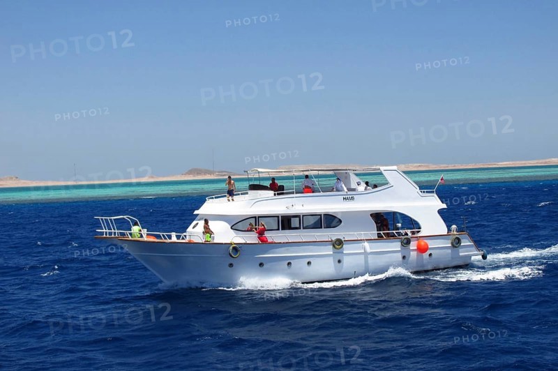 The snow-white yacht Hams, with a group of tourists on board, is enjoying a cruise on the Red Sea. The vessel is located near the Ras Mohammed Marine Reserve, where tourists and travelers enjoy diving and snorkeling. The desert and mountains of the Sinai Peninsula are visible in the background. South Sinai, Sharm el-Sheikh, Egypt