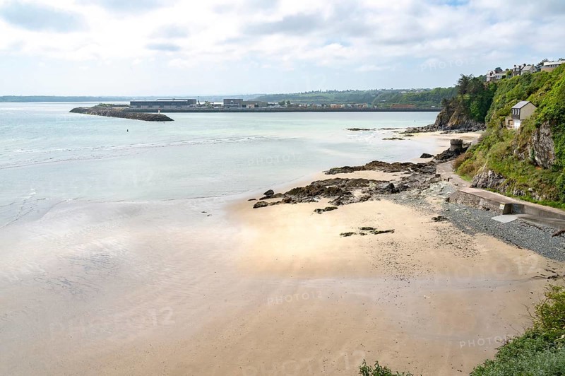 The view over a wide sandy and pebble beach at low tide towards the distinctive Port du Legue breakwater and the port area, while on the right a green coastal slope with isolated buildings slopes down to Anse aux Moines, Plerin, Saint-Brieuc Bay, Cotes-d'Armor, Brittany region, France