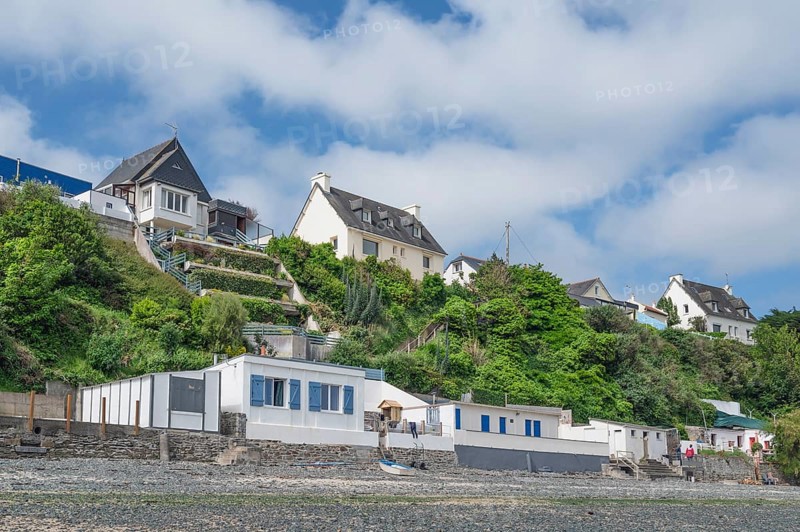 A series of colorful, historic beach cabins with walls of natural stone line the rocky beach at the foot of a steep slope, on which villas are enthroned, on the Plage des Nouelles, Plerin, Saint-Brieuc Bay, Cotes-d'Armor, Brittany region, France