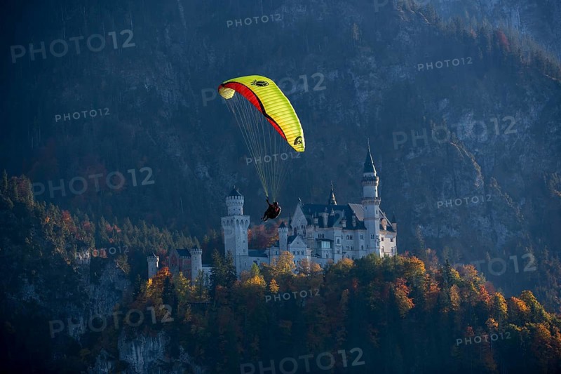 A paraglider flies in front of Neuschwanstein Castle in an autumn landscape, Schwangau, Ostallgäu, Allgäu, Swabia, Bavaria, Germany