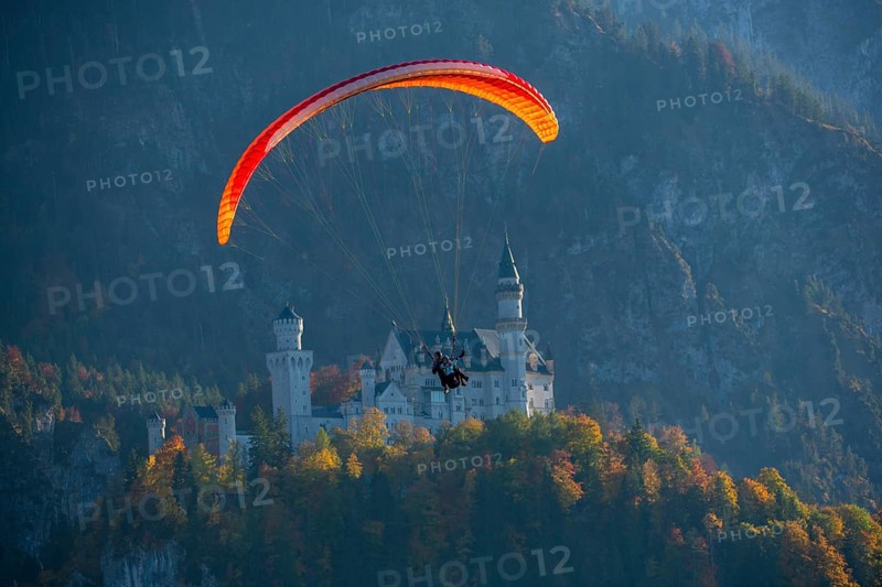Paraglider flies off Neuschwanstein, nestled in an autumn mountain landscape, Schwangau, Ostallgäu, Allgäu, Swabia, Bavaria, Germany