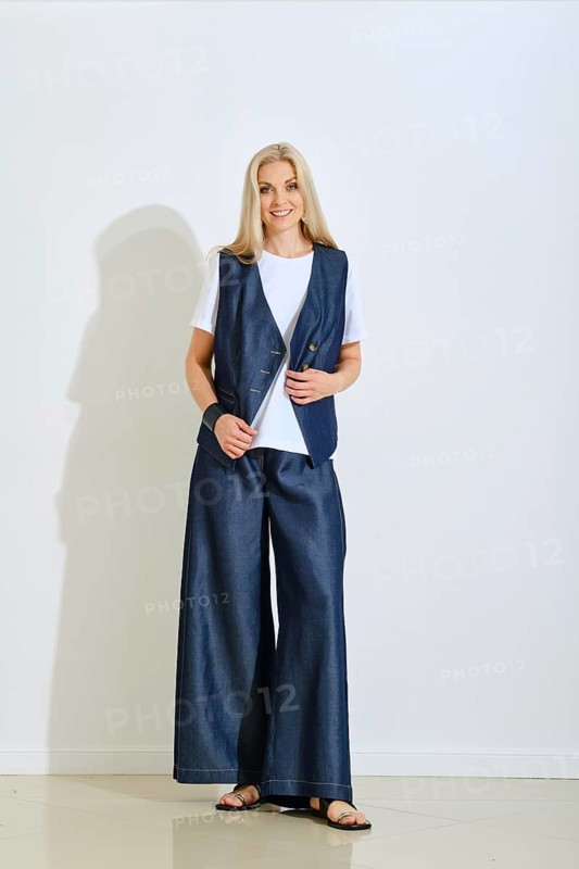 A woman stands confidently in a modern studio dressed in a denim vest and wide-legged pants. The light showcases her relaxed style, perfect for summer outings or casual gatherings