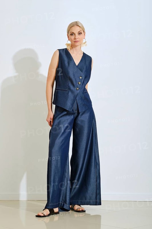 A woman models a fashionable navy vest and wide-leg pants in a contemporary studio. Natural light highlights her confident pose and the elegant design of her outfit