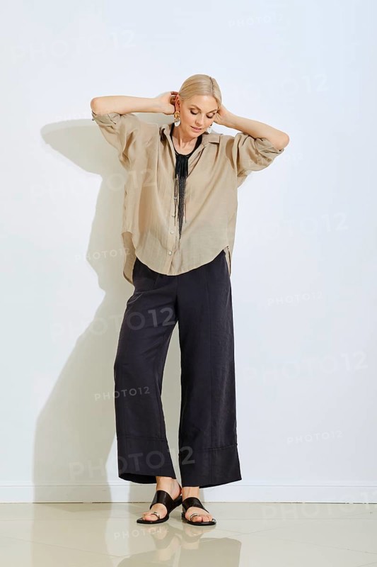 A model showcases a relaxed outfit consisting of a loose beige shirt and dark wide-leg pants