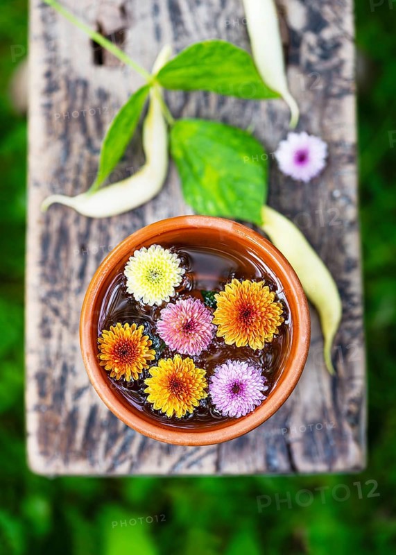 Bright chrysanthemum flowers in shades of yellow, orange and pink in a clay bowl with water. Placed on rustic wood, the composition reflects harmony, nature and simple beauty