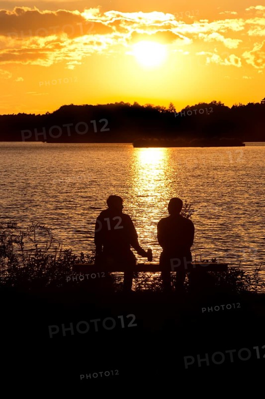 Two men sitting on a bench at sunset at Lake Gudelack, Lindow (Mark), Stechlin-Ruppiner Land nature park Park, Brandenburg, Germany