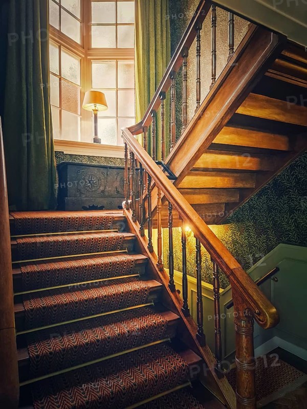 A vintage, wooden staircase with classic balusters leads up to a soft light that filters through the window. Warm, moody atmosphere, of an old hotel, Lisse, Holland, Netherlands