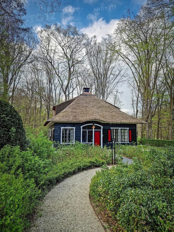 A winding paved path slopes down through the forest leading towards a rustic house nestled in the woods. Peaceful scene with secluded atmosphere, Lisse, Holland, Netherlands