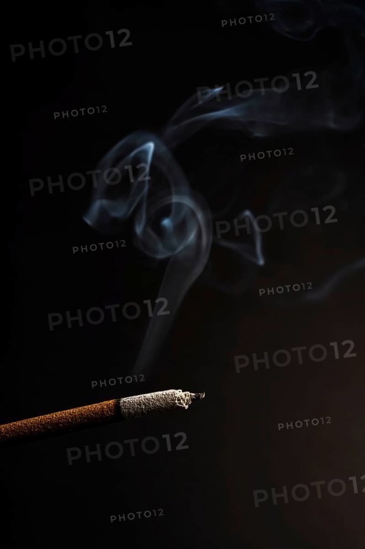 Close-up of a burning incense with white smoke coming out illuminated on a black background