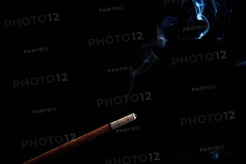Close-up of a burning incense with white smoke coming out illuminated on a black background