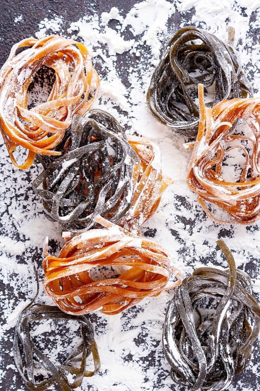 Pasta with carrots and spinach on a floured table, space for text