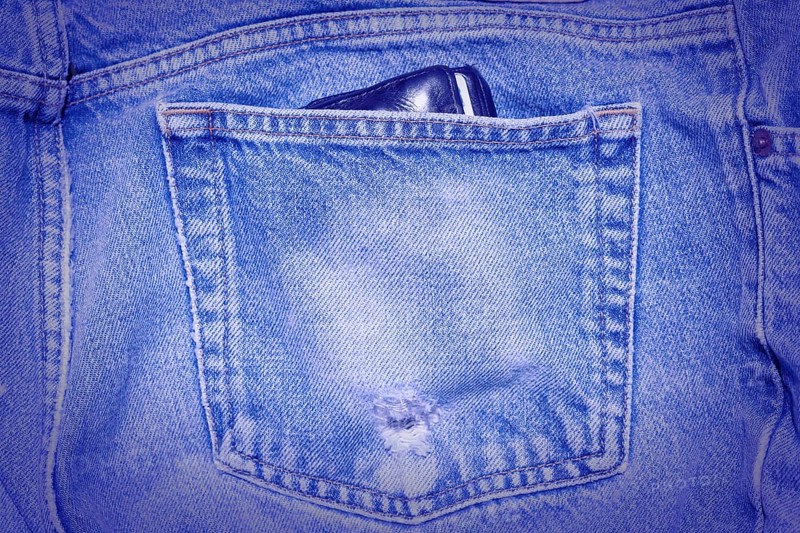 A Worn and tattered blue Jeans pocket. Carrying a wallet in your back pocket can hurt your back