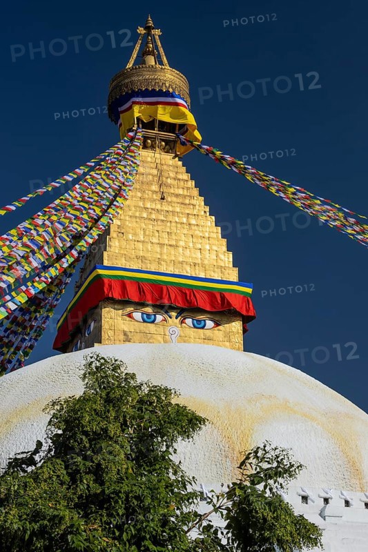 Boudhanath, the Boudha Stupa, the largest stupa in Nepal, Buddhist religious complex, UNESCO World Heritage Site and one of the main Kathmandu Valley tourist attractions. The upper part of the dome and the gilded, golden spire with Buddhist prayer flags stretched from the top. Eyes on the cubic part, the harmika, represent all-seeing, wisdom eyes of the Buddha. Seen in the afternoon on a clear, blue-sky, early autumn day. Kathmandu, Bagmati Province, Nepal