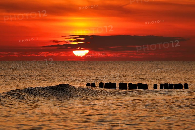 A vivid sunset over the sea with gentle waves and an orange sky creating a tranquil atmosphere. Baltic sea, Poland, Kolobrzeg