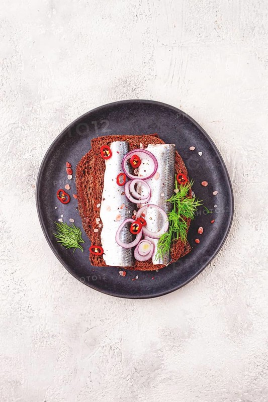 Sandwiches, herring fish, on dark rye bread, sprinkled with onion, chili pepper and herbs, on a dark plate