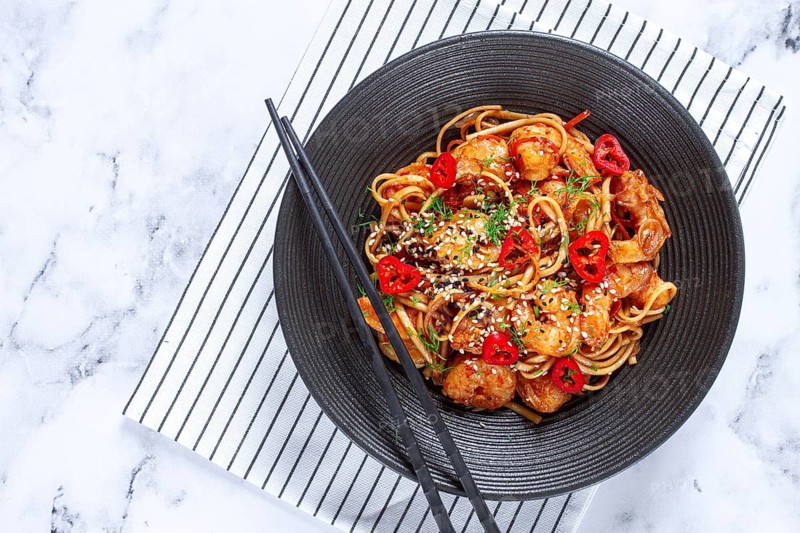 Delicious shrimp stir-fry with noodles and colorful vegetables served in a black bowl on a striped napkin
