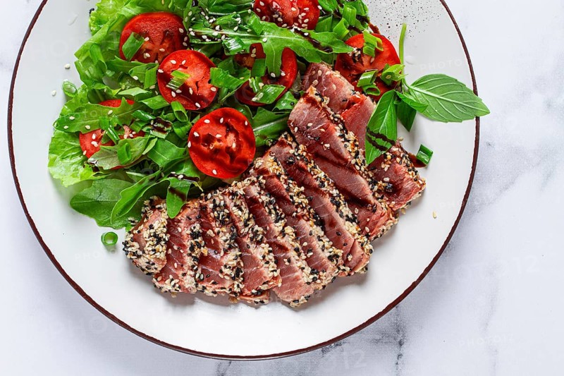 Fried tuna in sesame seeds, sliced on a plate, with fresh salad, on a white plate, homemade