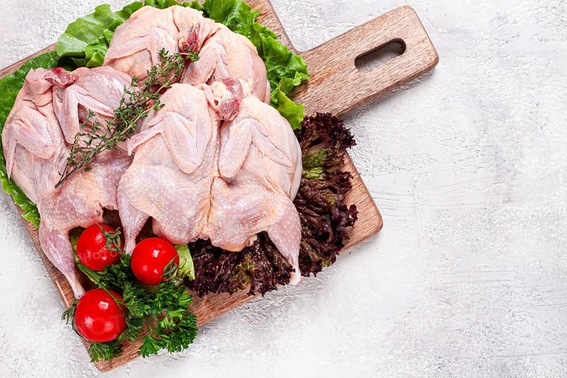 Raw quail meat, three quail carcasses, on a wooden chopping board, garnished with lettuce and herbs
